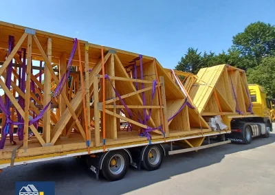 Yellow Wyckham Blackwell truck hauling wooden roof trusses on a flatbed trailer.
