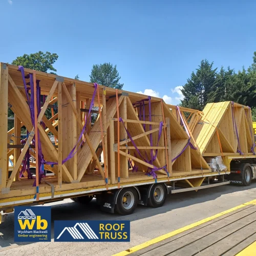 Yellow Wyckham Blackwell truck hauling wooden roof trusses on a flatbed trailer.