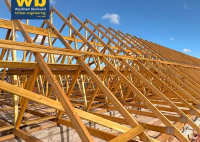 Rows of timber Roof Trusses on a building under a clear blue sky, Wyckham Blackwell logo in top left.